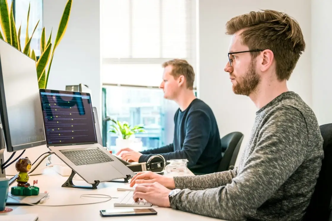 Two software engineers working together at their monitors in a bright office